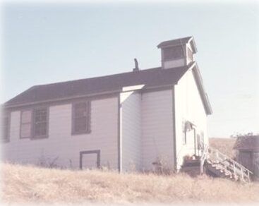 A picture looking up at Seaside School from the driveway. The school is white with green trim.